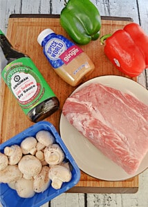 A pork roast, a container of mushrooms, a pepper, a bottle of soy sauce, a container of ginger.