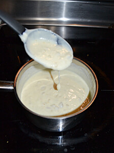 A saucepan with white enchiladas sauce and a spoon drizzling the sauce back intot he pan.