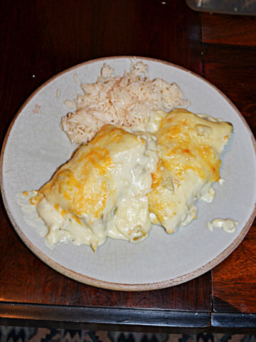 A plate with two white chicken enchiladas topped with cheese and a side of rice.