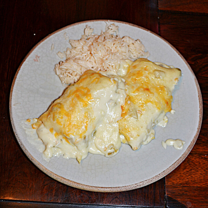 A plate with two white chicken enchiladas topped with cheese and a side of rice.
