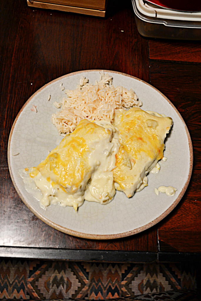 A plate of two white chicken enchiladas with rice on the side.