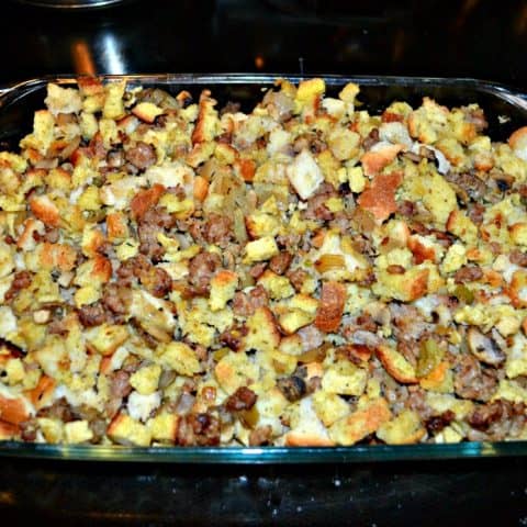 A pan filled with white and yellow cornbread cubes, pieces of mushrooms, sausage, and vegetables, sitting on a stove.