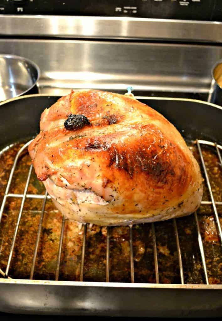 A golden brown turkey breast sitting on a rack in a roasting pan.