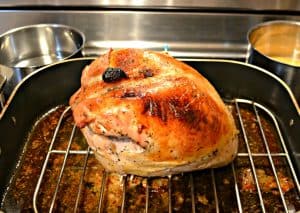 A golden brown turkey breast sitting on a rack in a roasting pan.