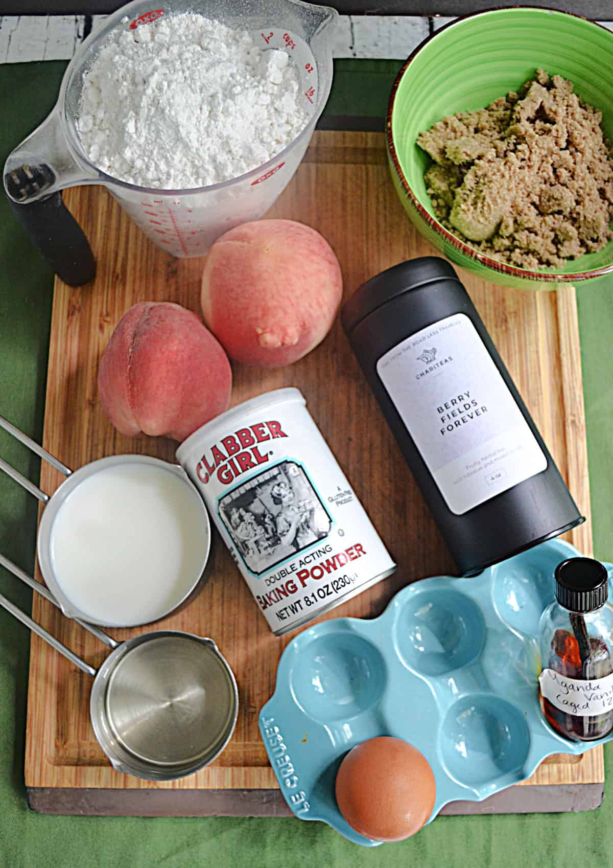 Cutting board with beaches, flour, tea, milk, sugar, and eggs on it.
