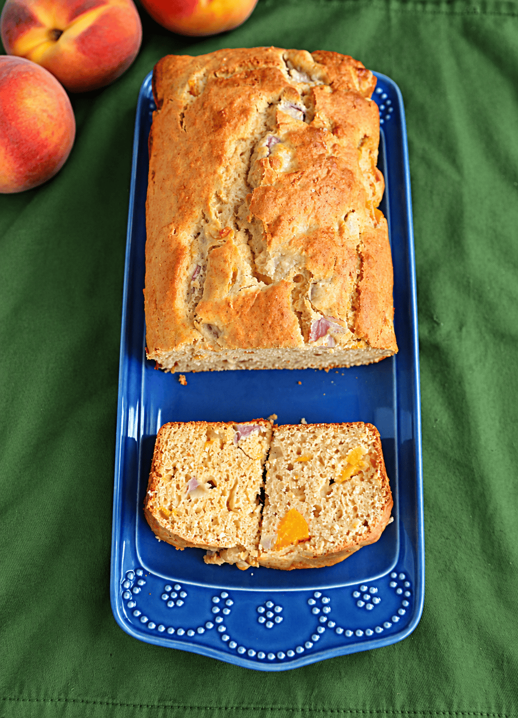 A loaf of bread with a piece cut off and peaches behind it.