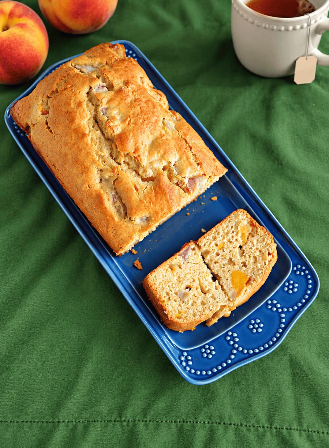 A loaf of bread with peaches and a cup of tea behind it.