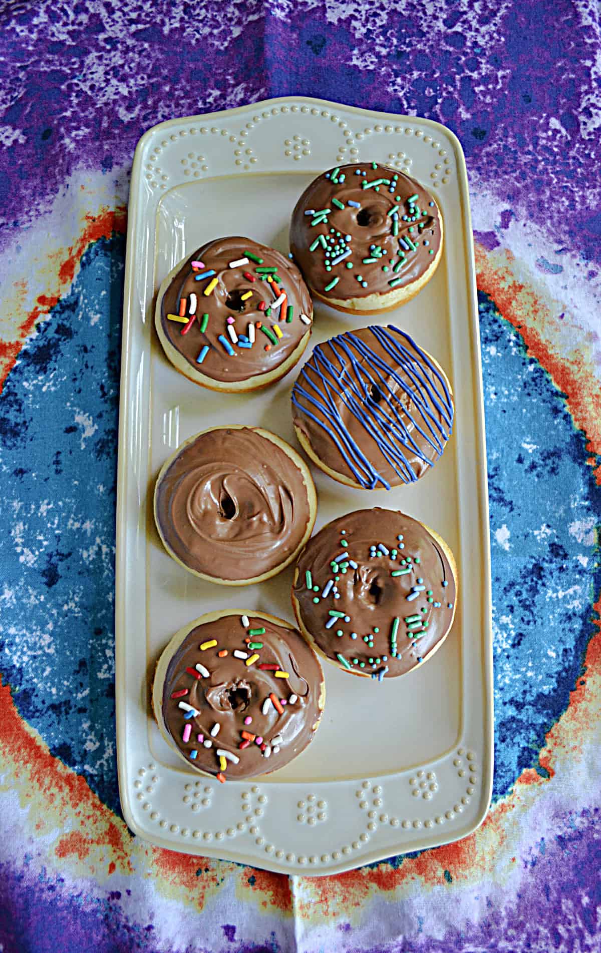A platter with six chocolate glazed donuts on it.