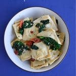 A close up view of a bowl of ravioli topped with spinach and bacon.