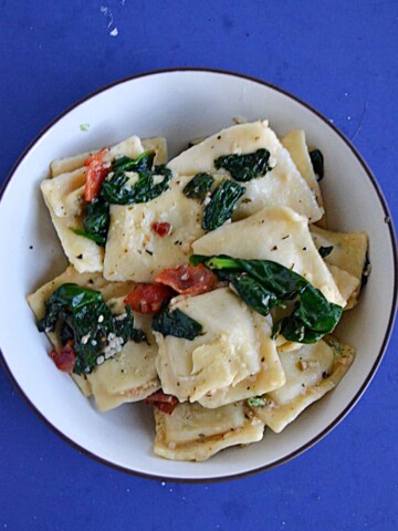A close up view of a bowl of ravioli topped with spinach and bacon.