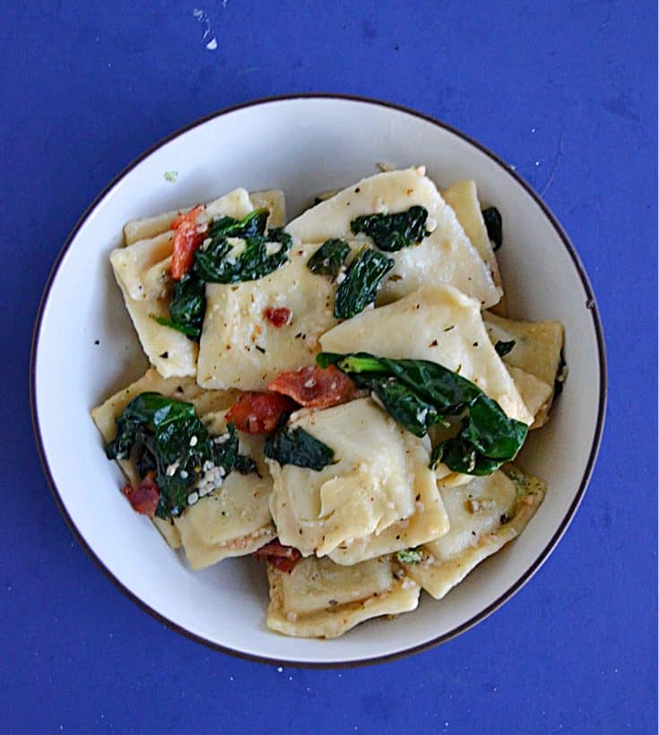 A close up view of a bowl of ravioli topped with spinach and bacon.