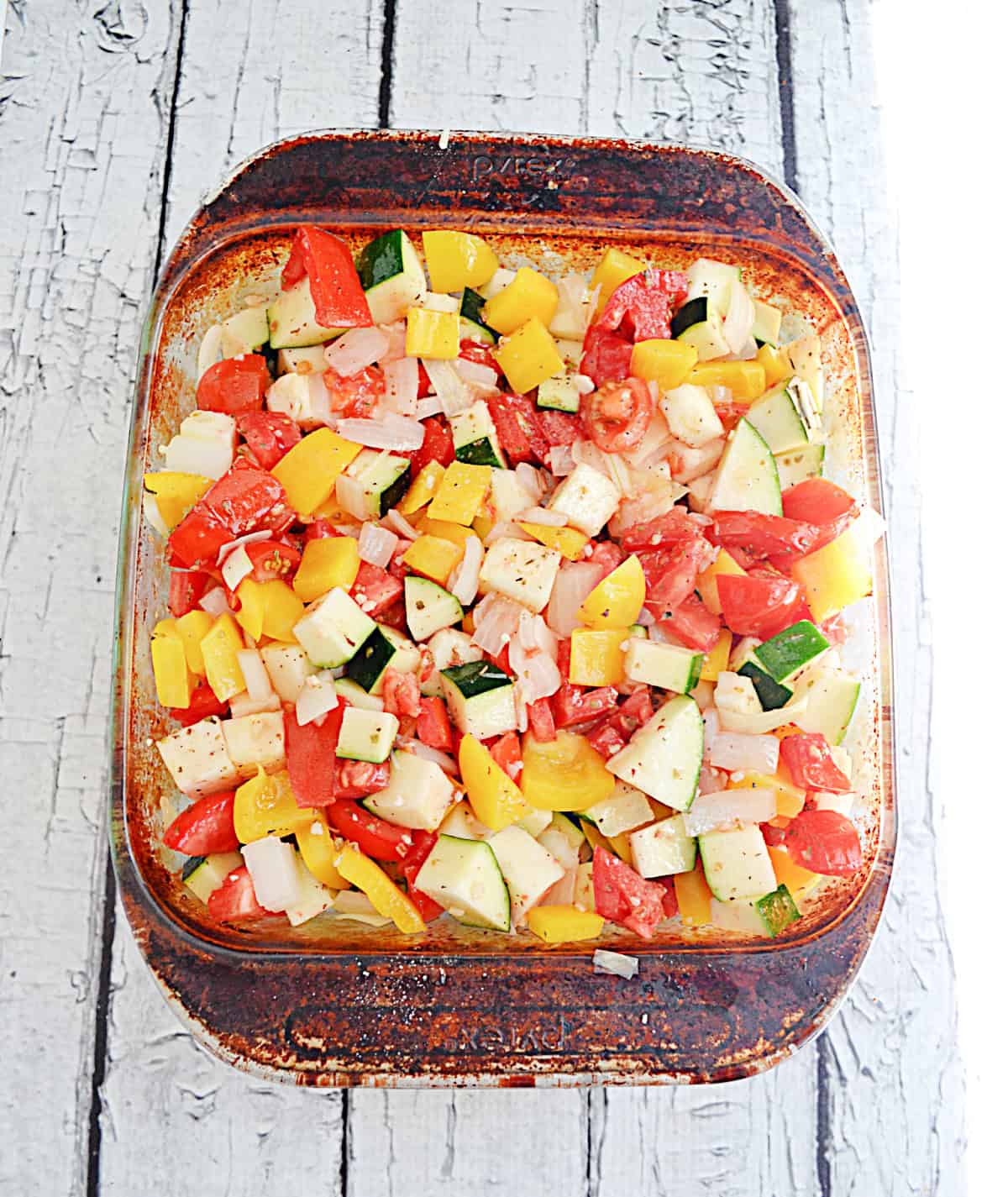 A baking dish with diced tomatoes, zucchini, and bell peppers in it.