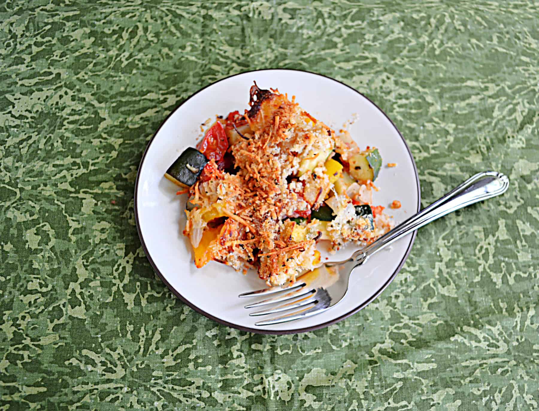 A plate of vegetables topped with cheese with a fork on the plate.