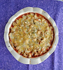 A pie pan filled with chicken, sauce, and cheese.