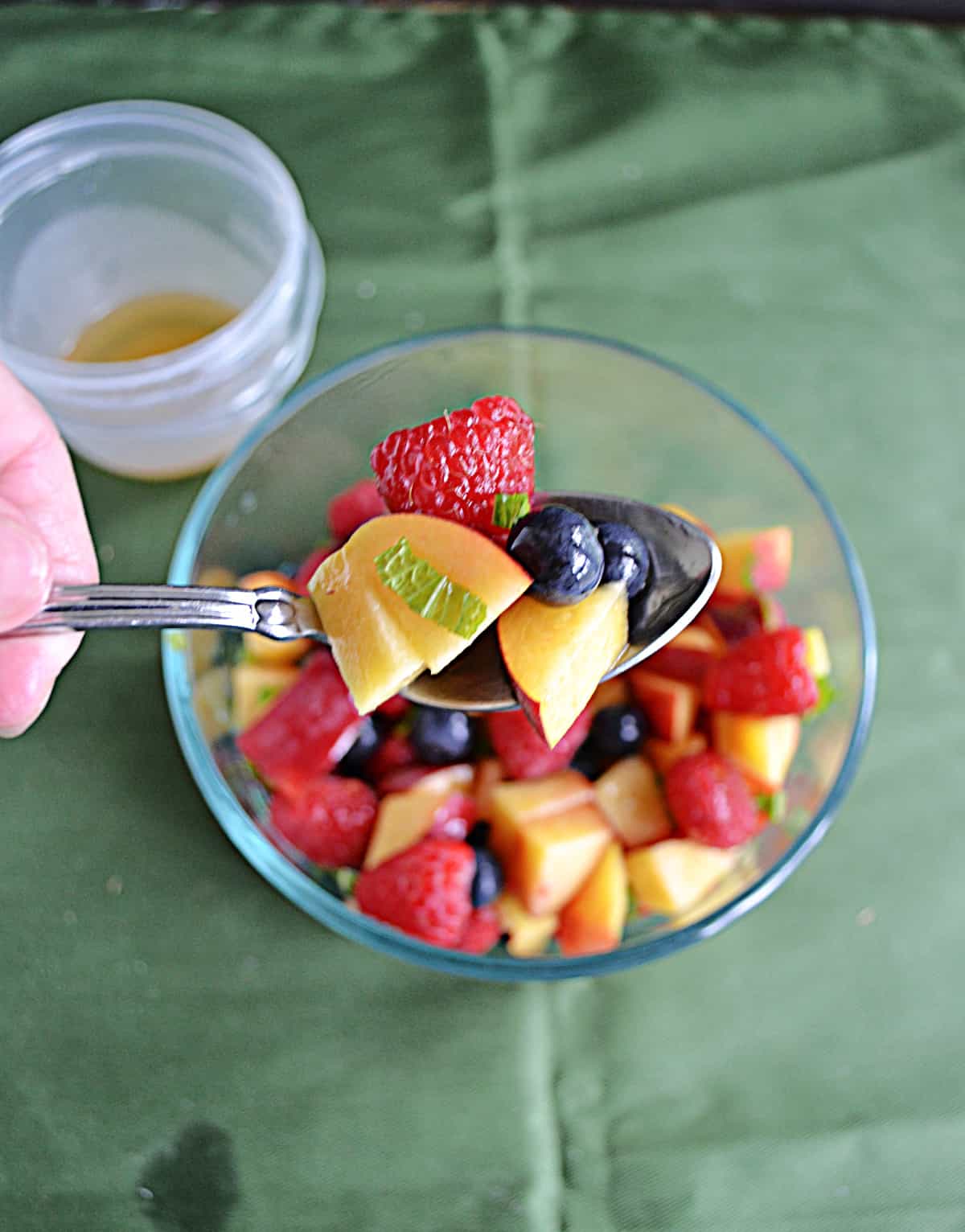 A bowl of fruit with a spoon holding some of it up.