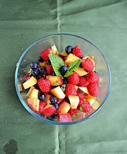 A bowl of fruit with a mint leaf on top.