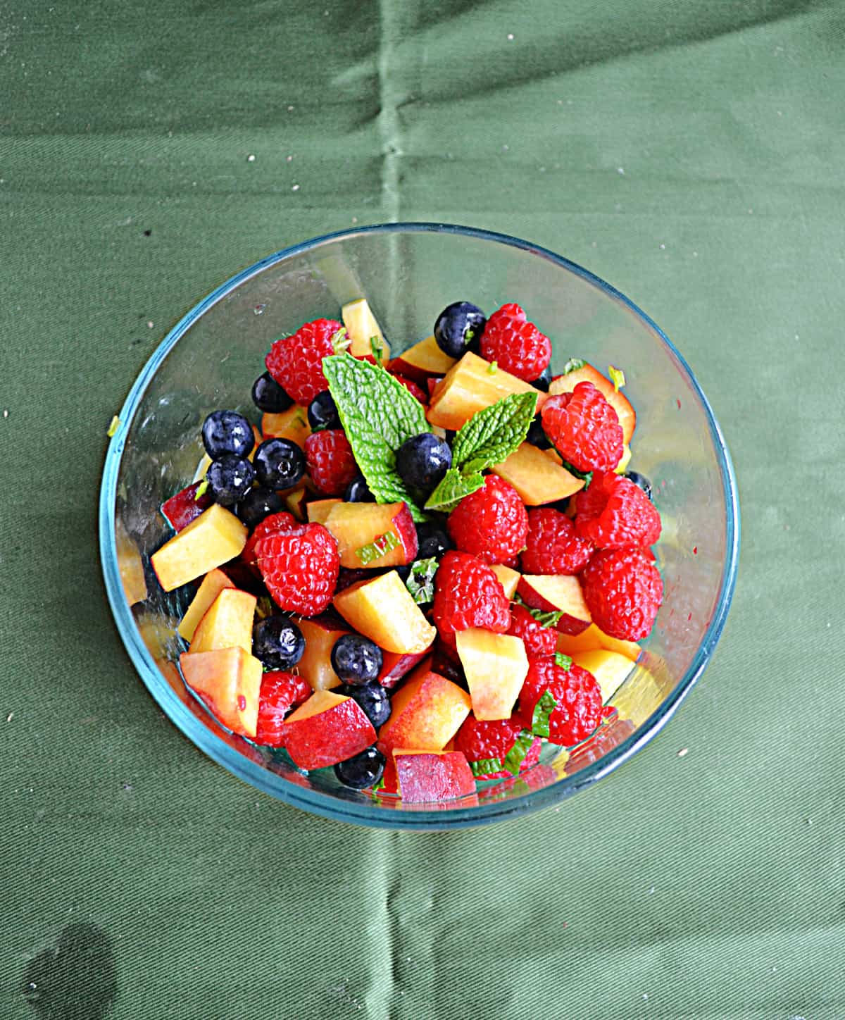 A bowl of fruit with a mint leaf on top. 