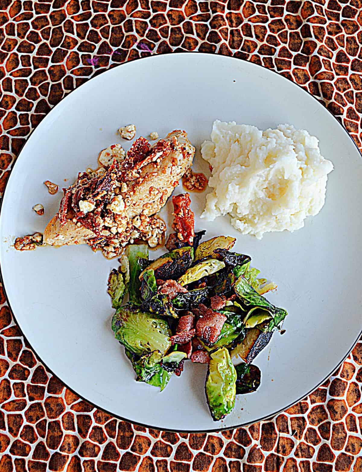 A top view of a plate with chicken and tomatoes, potatoes, and Brussels sprouts.