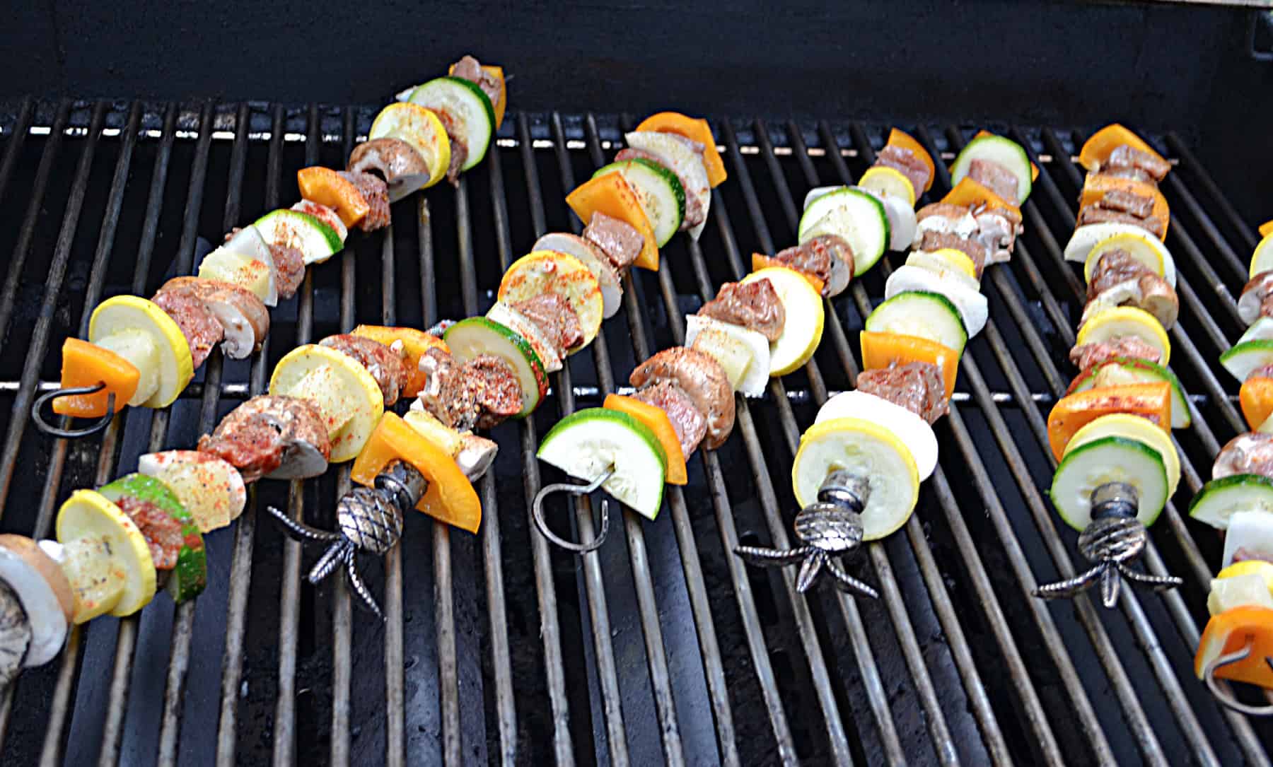 A grill with several beef and vegetable skewers on it.