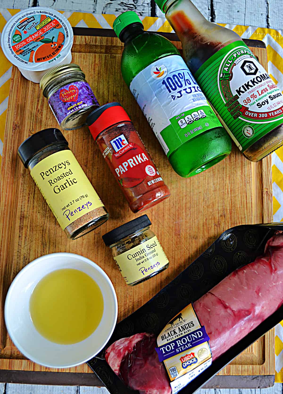 A cutting board with a steak, spices, butter, soy sauce, and fruit juices on it.