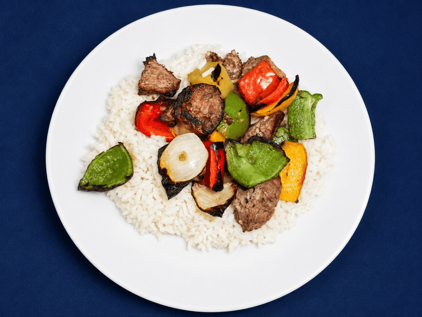 A plate with rice and a variety of colorful vegetables and grilled beef on it.