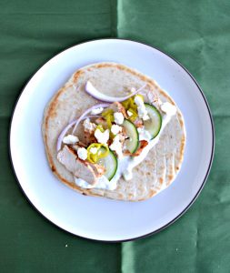 Pita bread topped with grilled chicken, cucumber, and red onions on a plate.