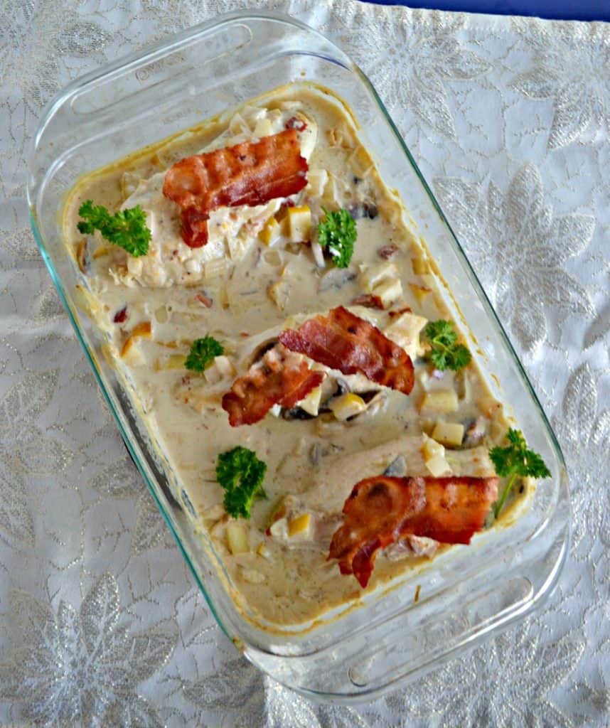 A baking dish with three chicken breasts topped with crispy bacon in a creamy sauce mixture then sprinkled with parsley on top.