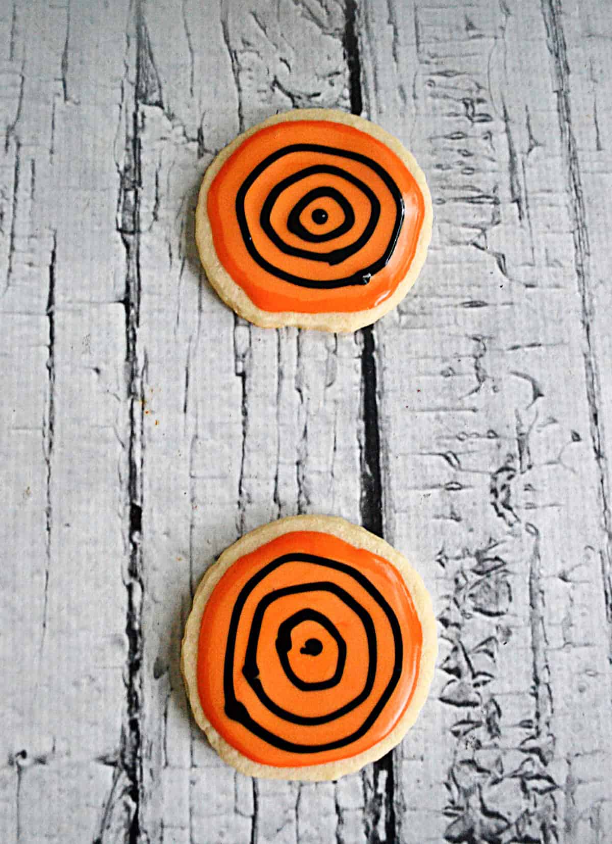 Sugar cookies with orange icing and a black swirl on them.