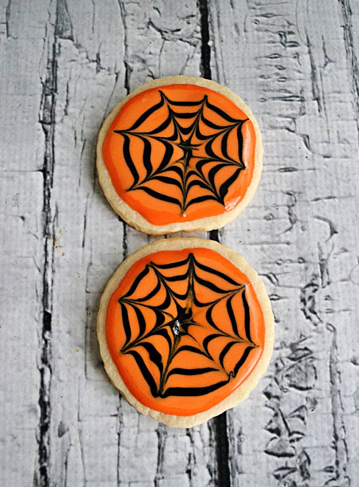 Orange frosted cookies with black spider webs on them. 