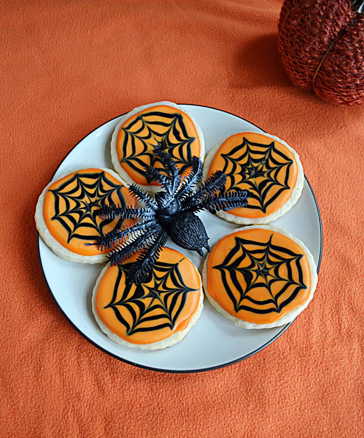 A plate of sugar cookies with orange frosting and black icing spider webs on them.