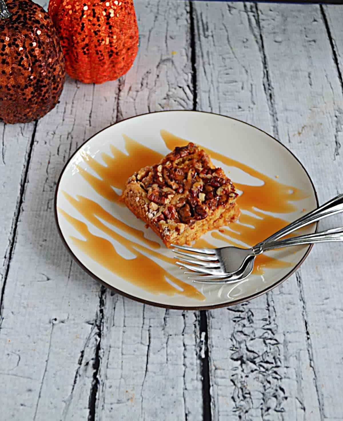 A plate with a slice of pumpkin cake with a caramel drizzle and two forks.