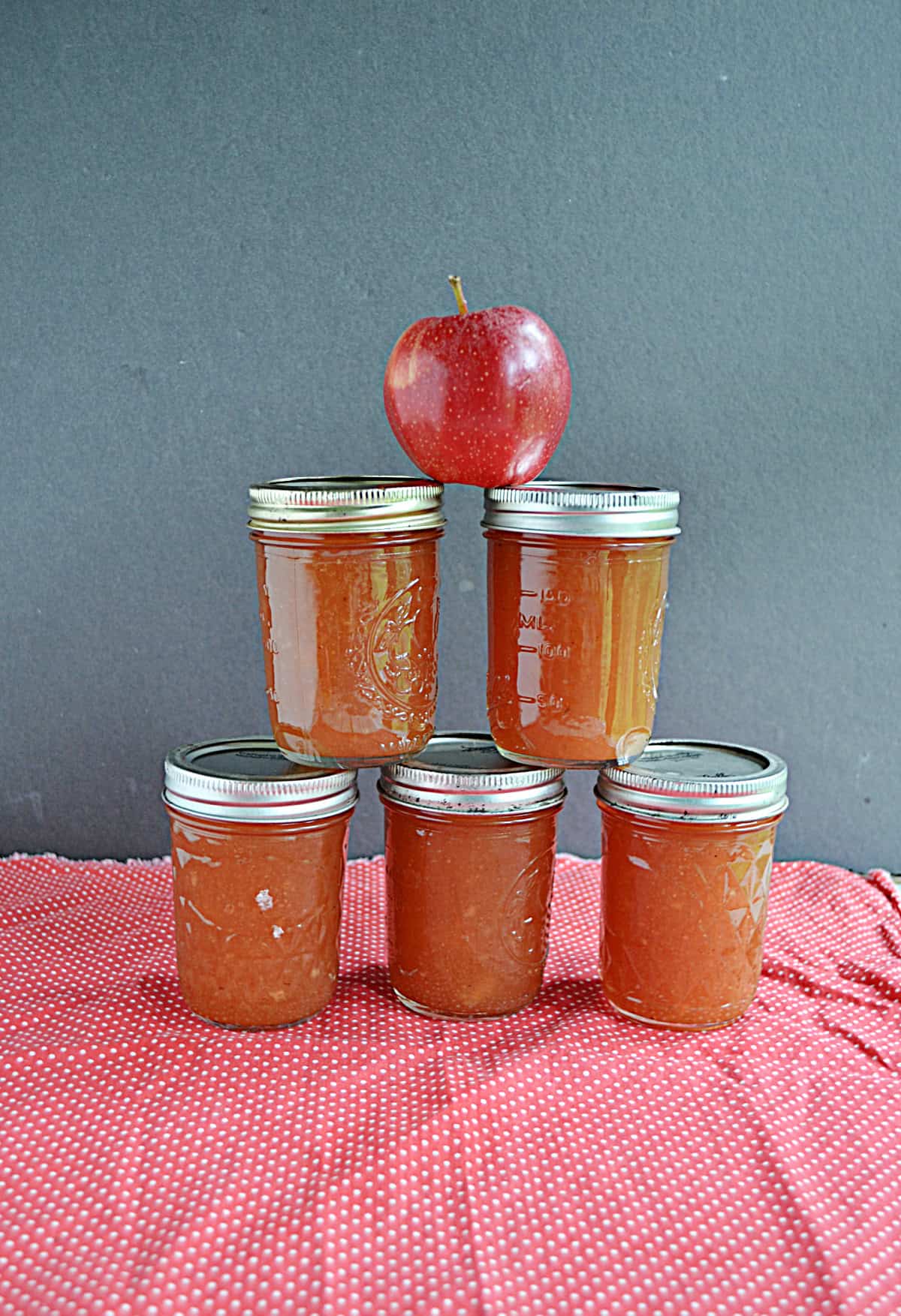 Jars of apple butter stacked on top of each other with an apple on top.