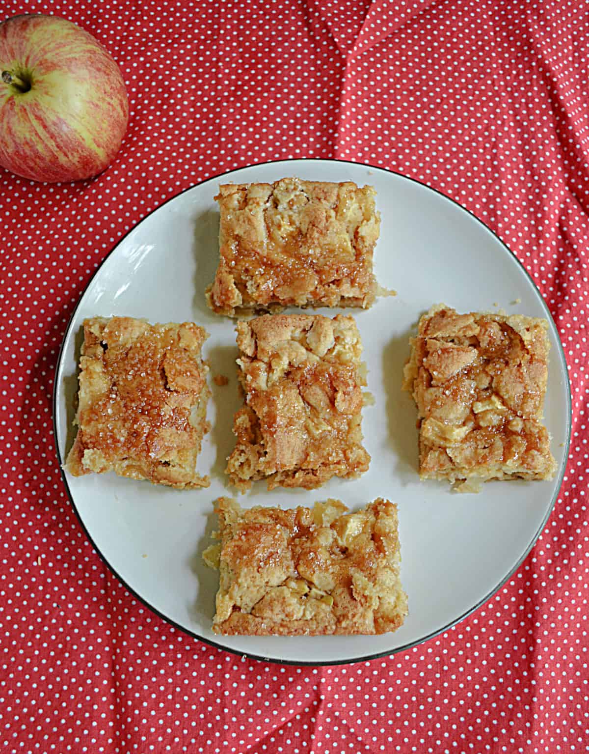 A plate of apple squares with apples behind the plate.
