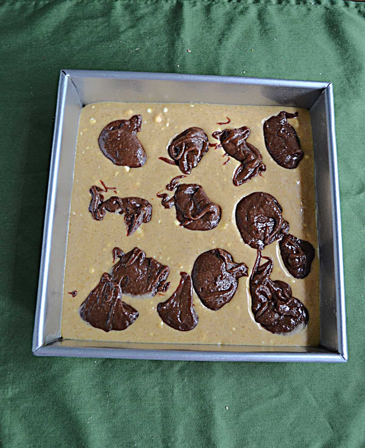 A pan of pumpkin cheesecake batter with dobs of brownie batter.