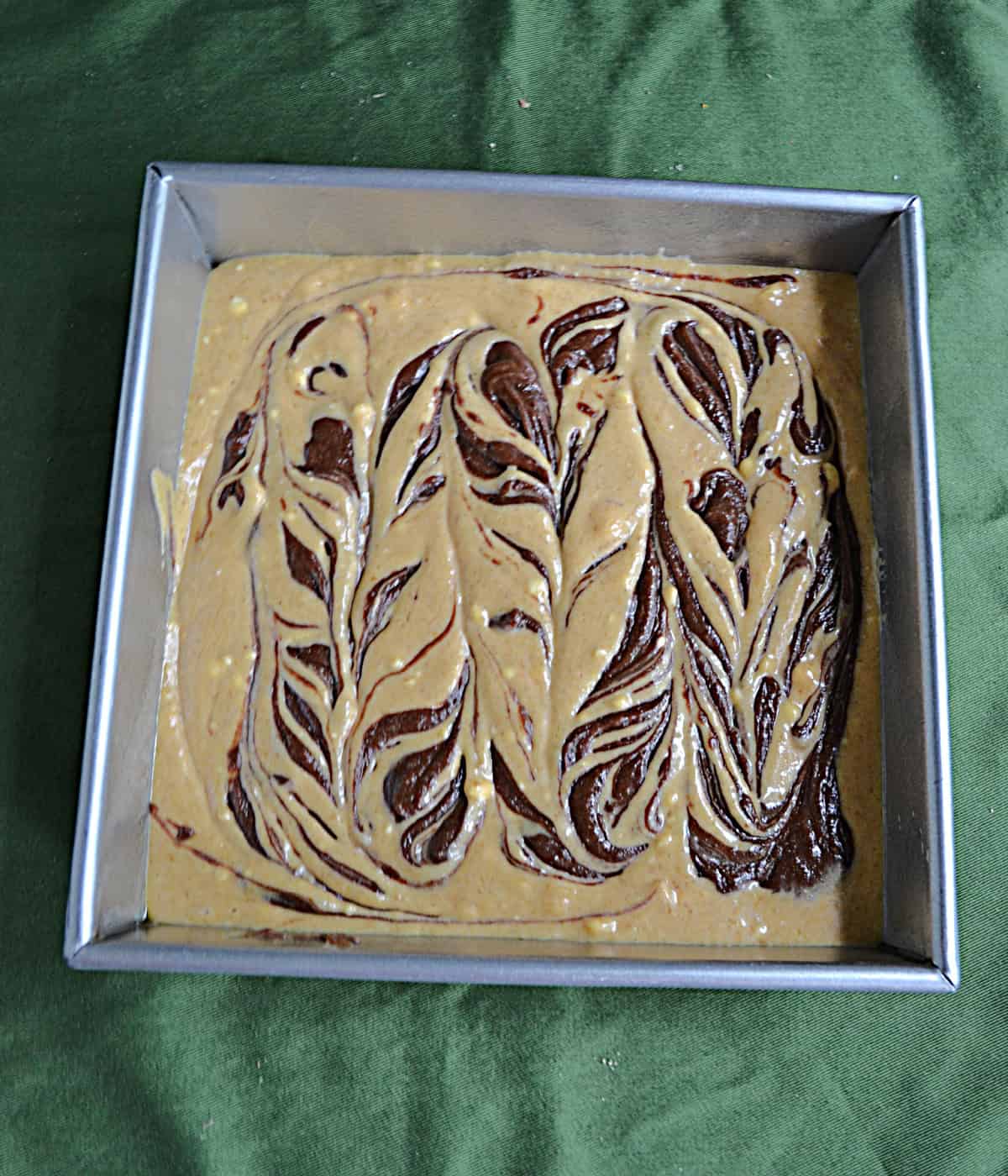 A swirl of pumpkin cheesecake batter and brownie batter in a pan.