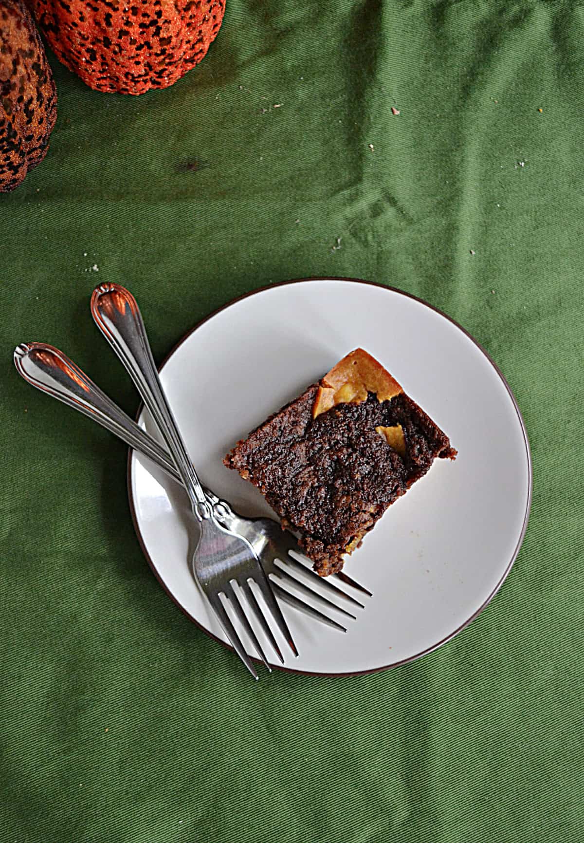 A plate with a brownie and two forks on it and two pumpkins behind the plate.