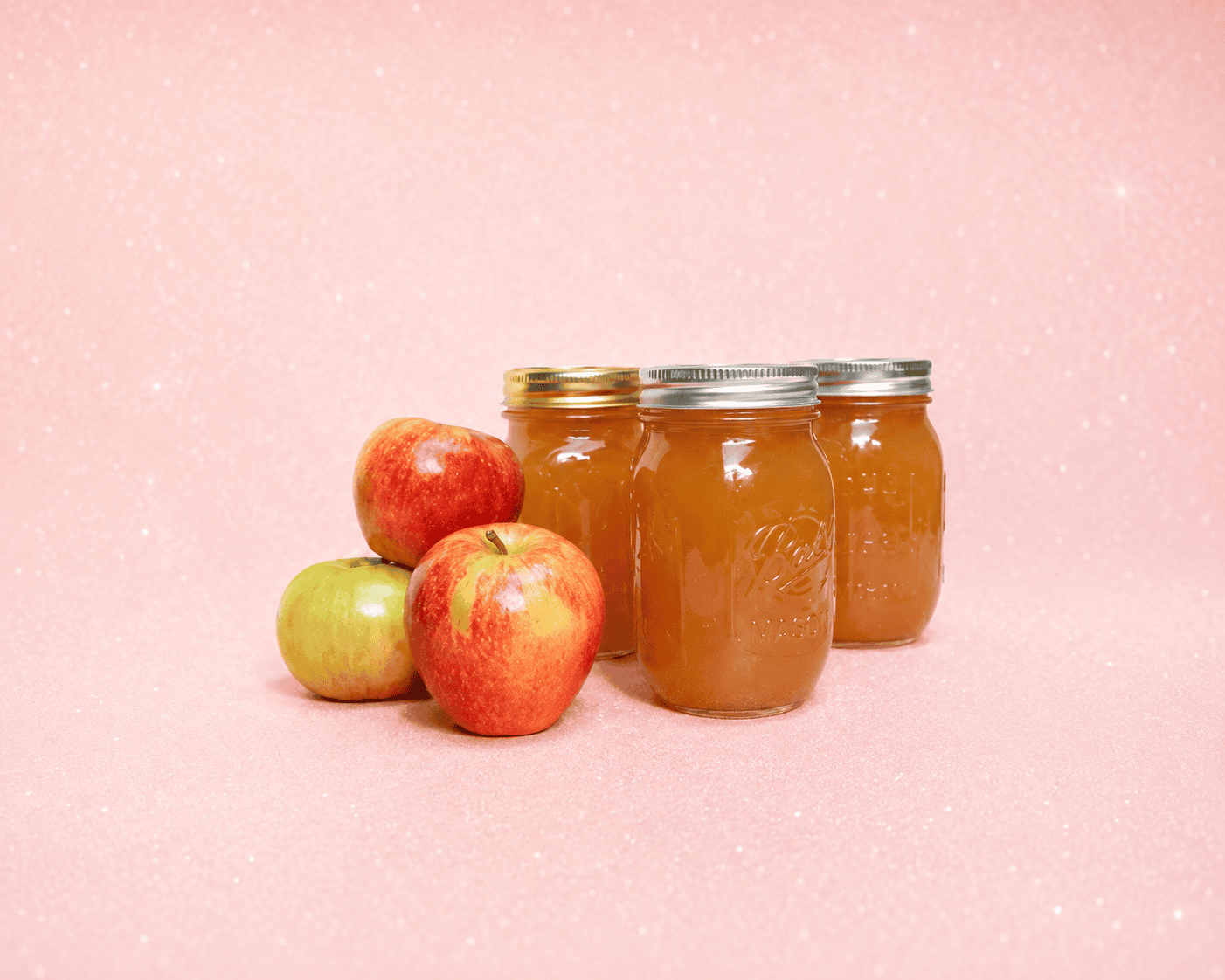 Jars of apple butter with 3 apples beside it.