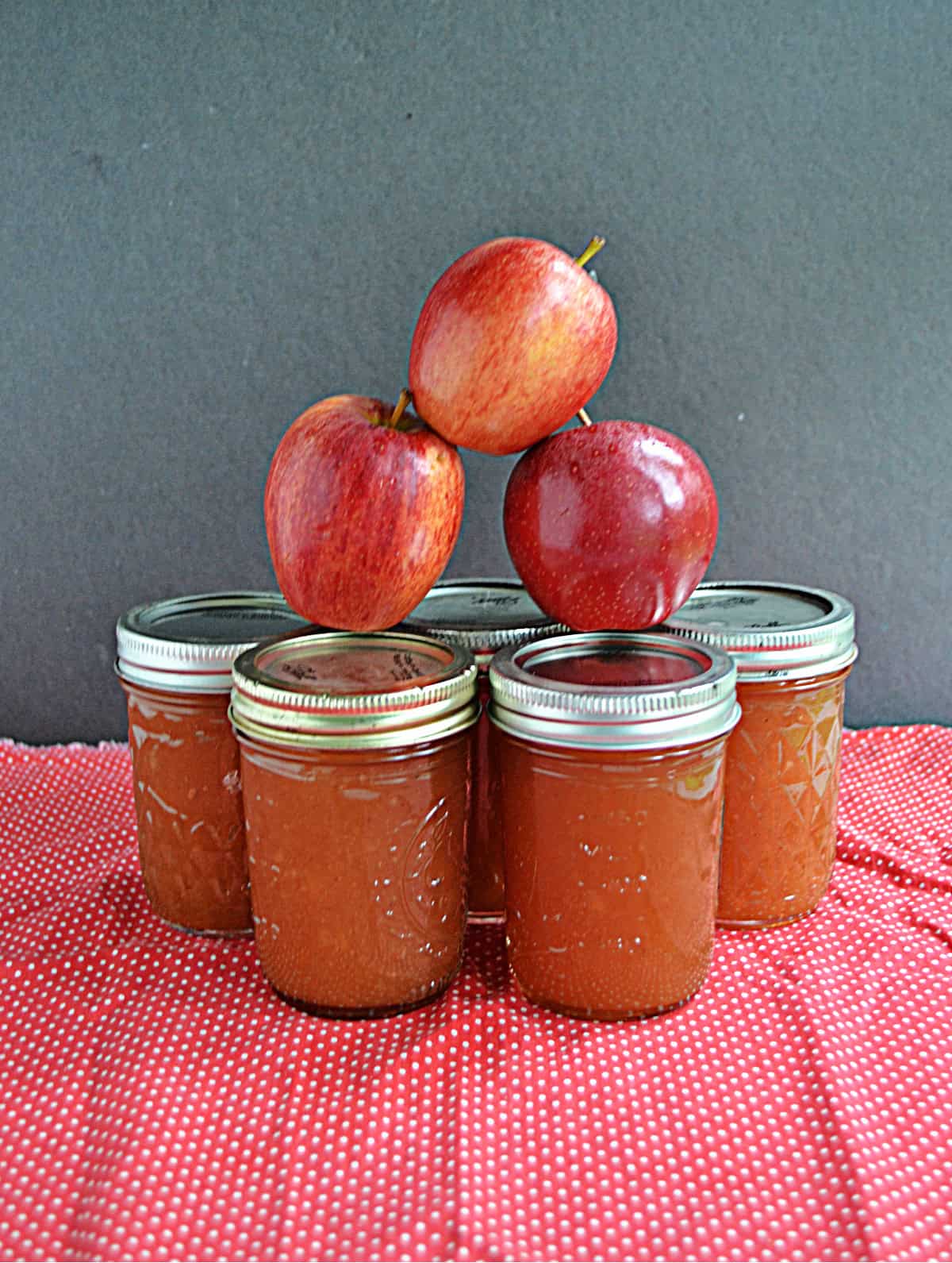 Jars of apple butter with apples stacked on top.
