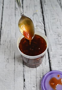 A spoon dripping Jack Daniel's Sauce into a container of sauce.