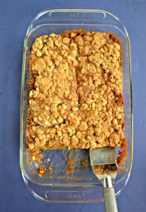 A pan of oatmeal cookie bars topped with a crumble, the first layer of cookies has been taken out and a metal spatula is in the pan.
