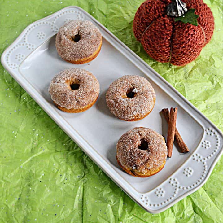 A platter with 4 pumpkin donuts rolled in autumn spice sugar with a pumpkin in the background.