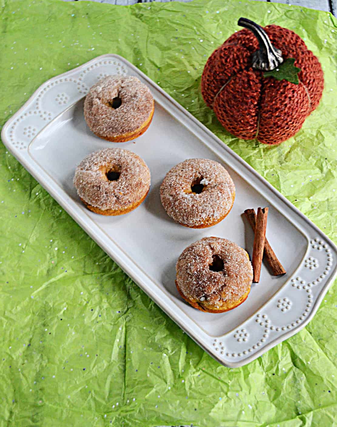 A platter with 4 pumpkin donuts rolled in autumn spice sugar with a pumpkin in the background.