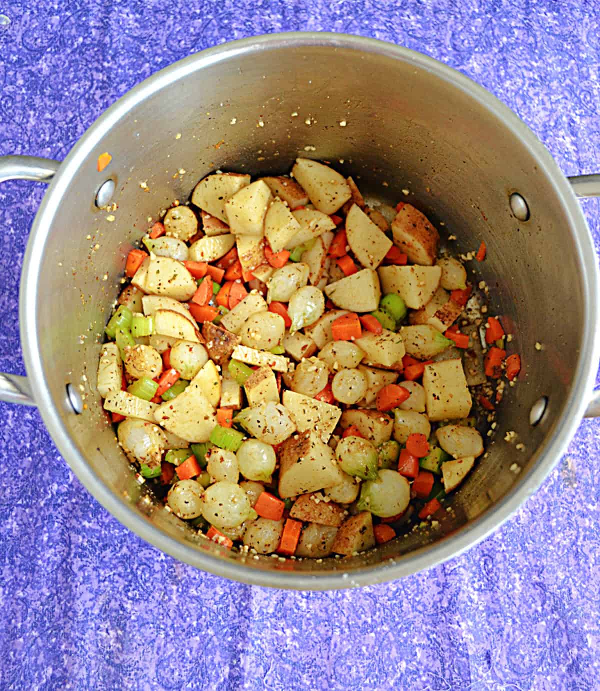 A stock pot filled with potatoes, onions, carrots, and celery.