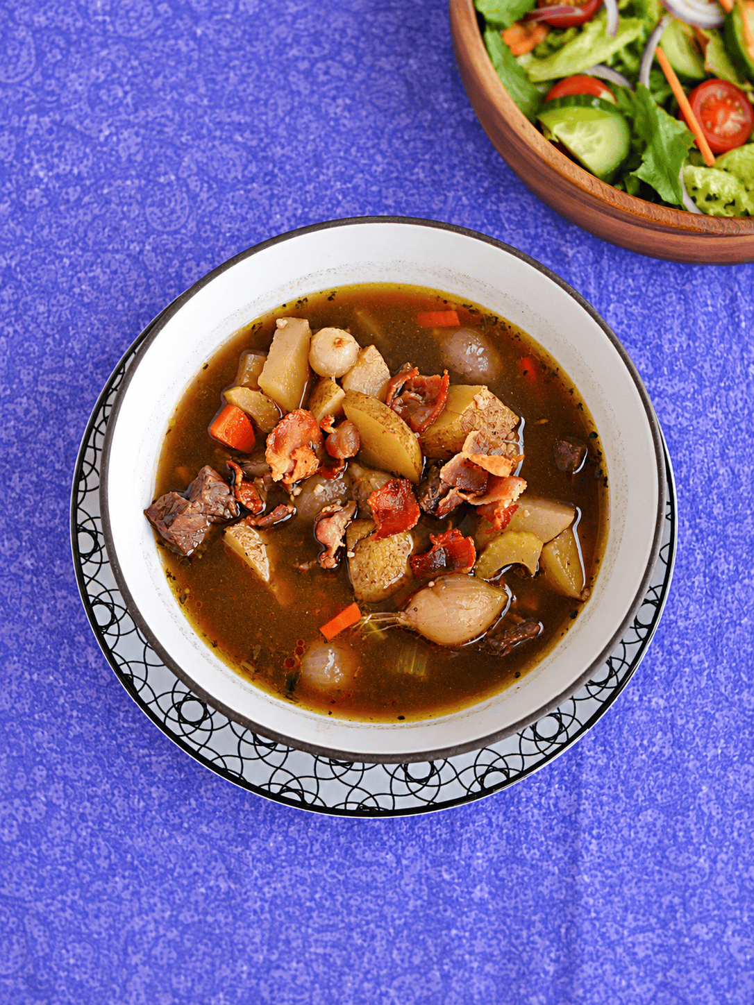 A bowl of beef Burgundy soup with a bowl of salad in the background.