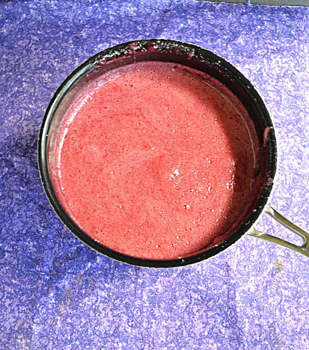 A pot of cherry jam with foam on top.