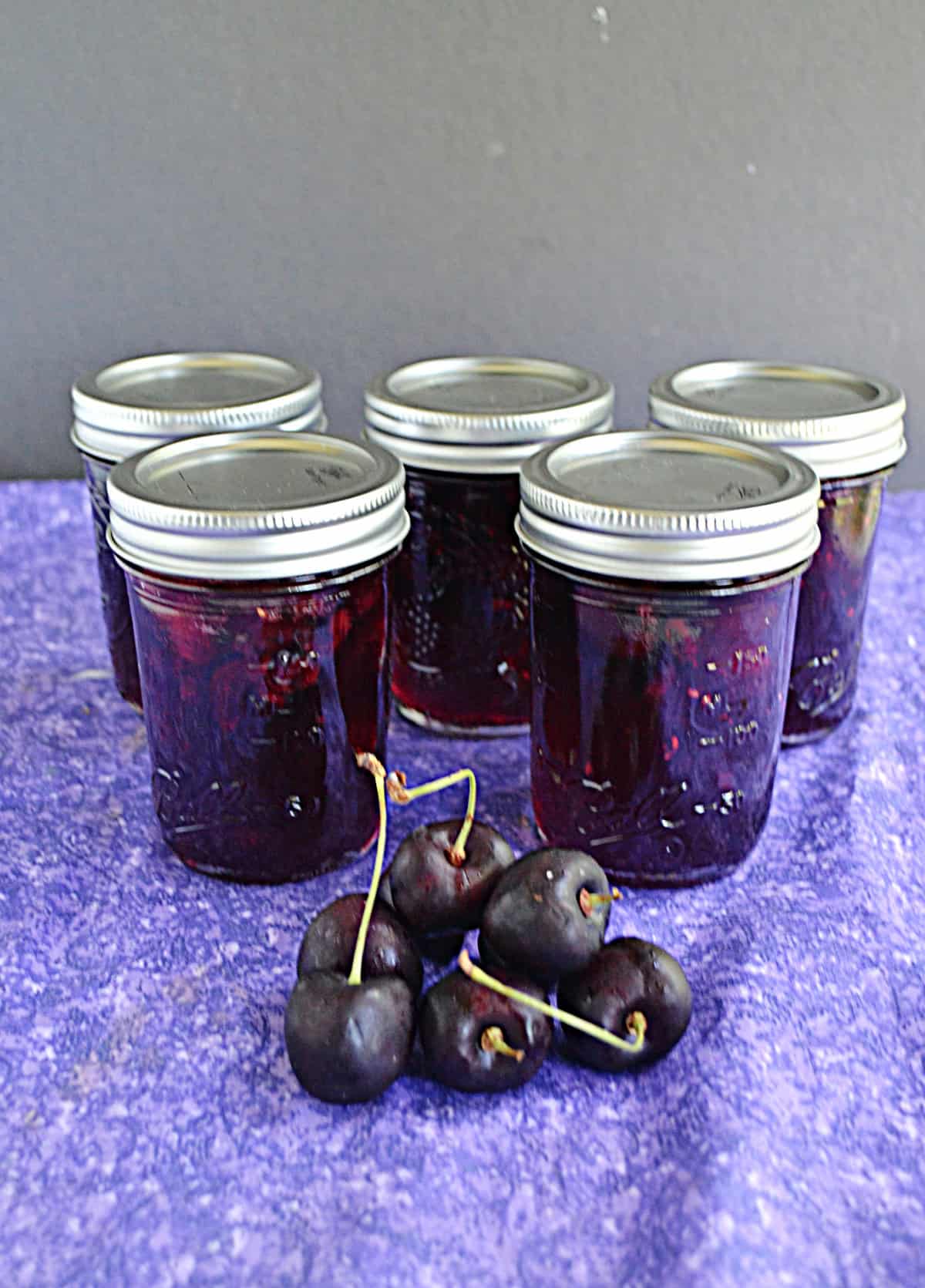 Jars of cherry jam with a pile of cherries in front of them.