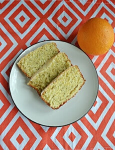 A plate with 3 slices of orange bread and an orange behind the plate.