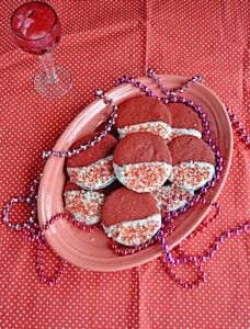 A plate of red velvet shortbread cookies dipped in white chocolate with beads on the plate.