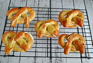 A cooling rack with 5 golden brown soft pretzels on it.
