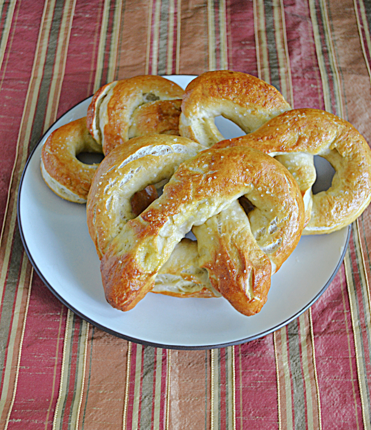 A plate with 3 large, golden brown pretzels on it.
